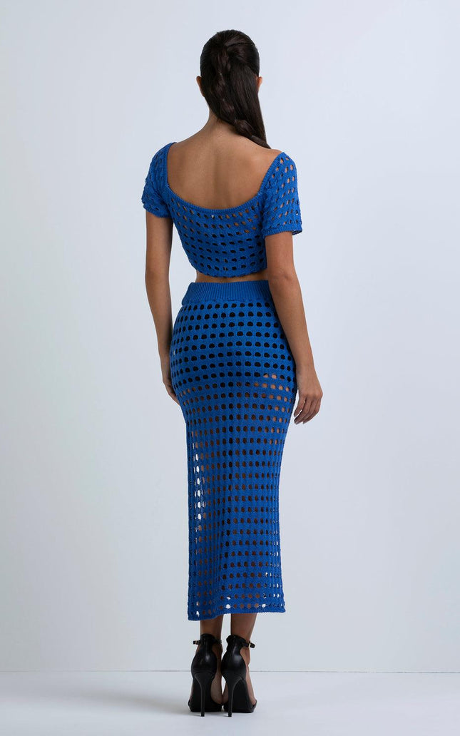 Woman in bold blue crochet two-piece outfit with short sleeves and skirt, back view