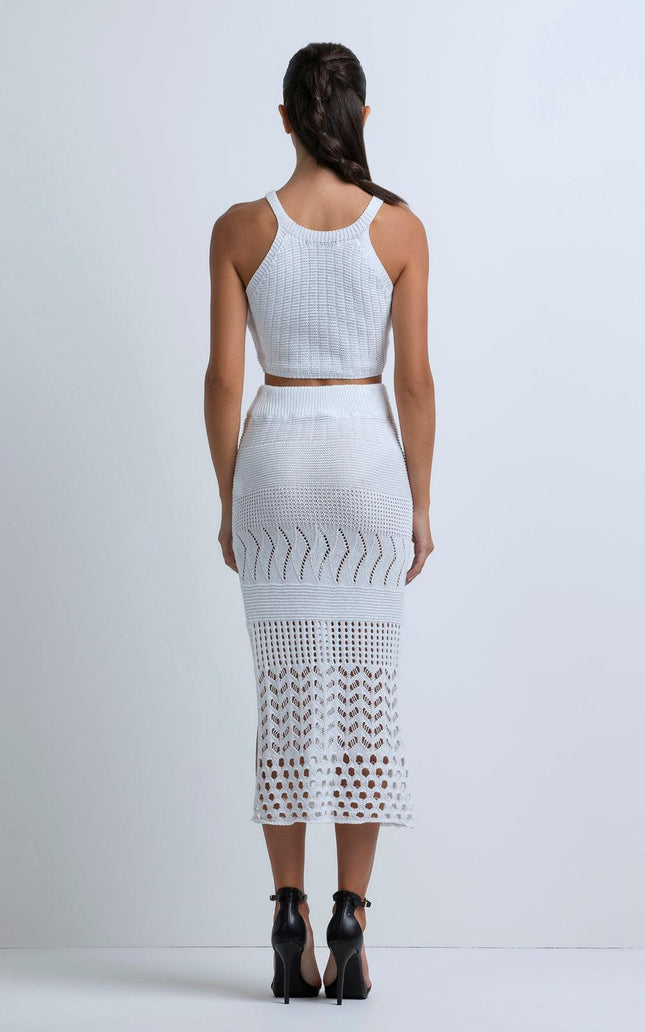 Woman in white knit crop top and midi skirt with lace pattern, back view.