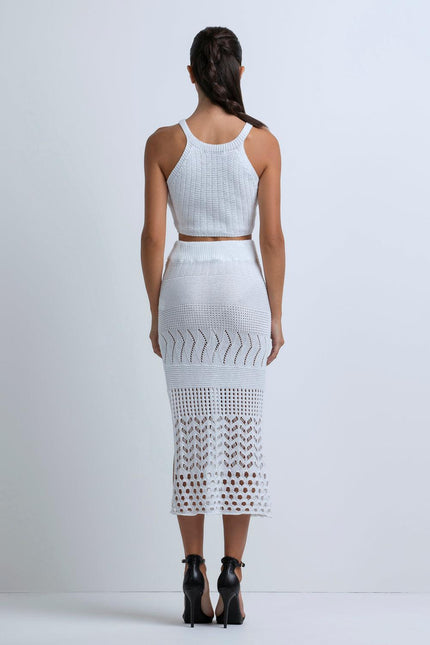 Woman in white knit crop top and midi skirt with lace pattern, back view.