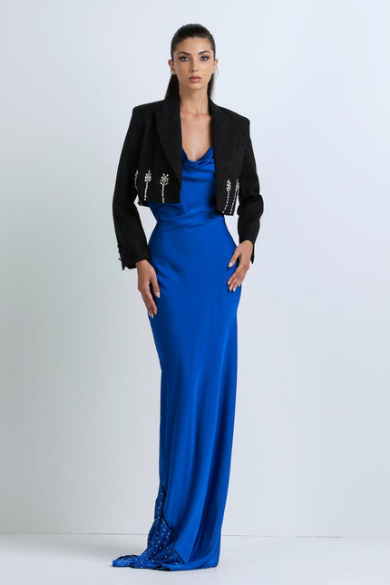 Woman wearing a royal blue satin evening gown and cropped black jacket with jeweled accents