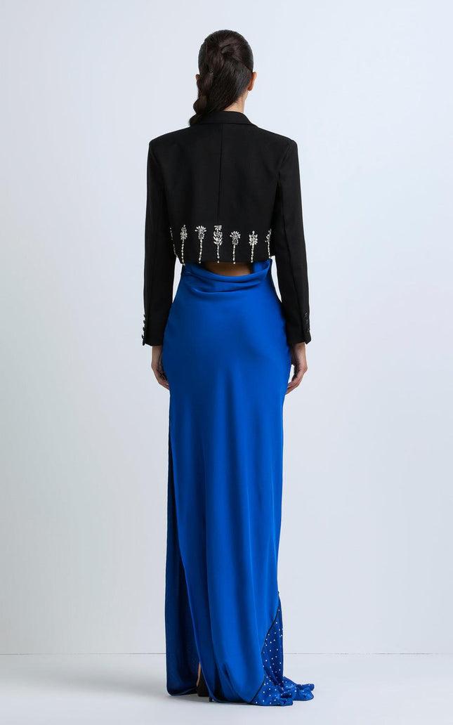 Woman in black cropped jacket with crystal details and royal blue maxi skirt, back view