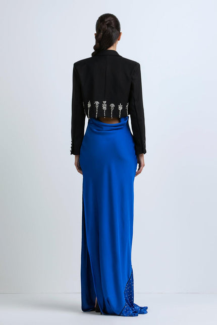 Woman in black cropped jacket with crystal details and royal blue maxi skirt, back view