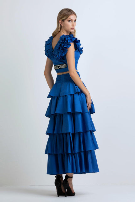 Woman in ruffled blue skirt set with crop top, open back, and crystal belt detail