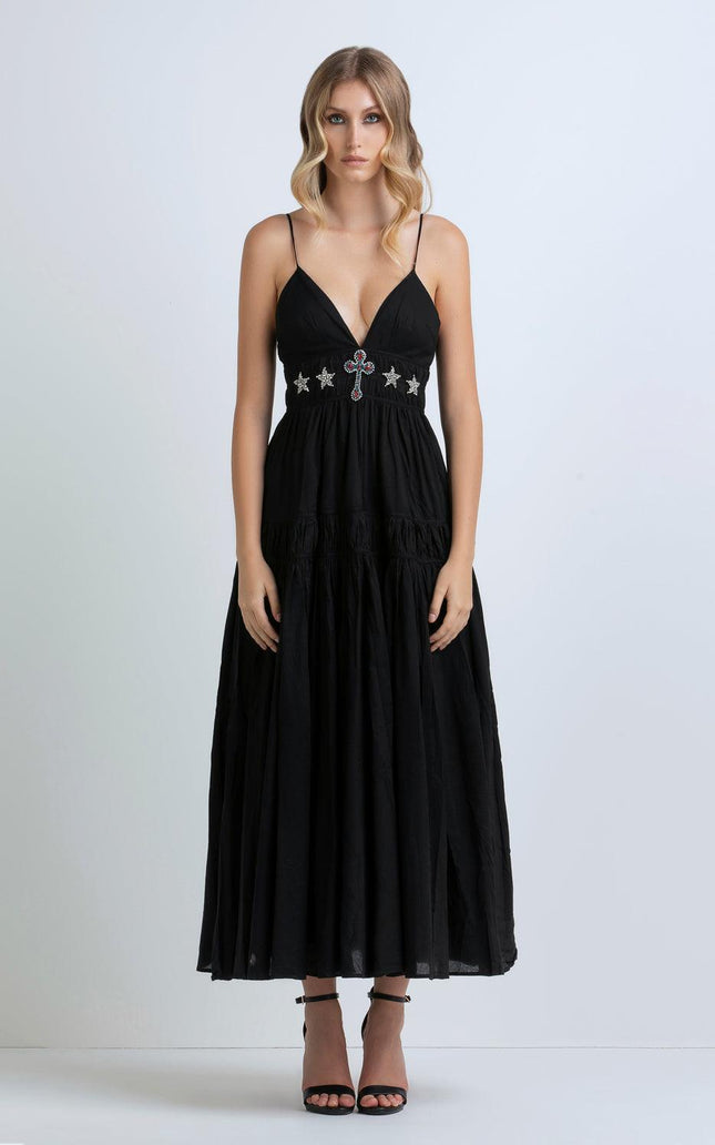 Woman wearing a black maxi dress with deep V-neck, jeweled cross and star detailing, thin straps