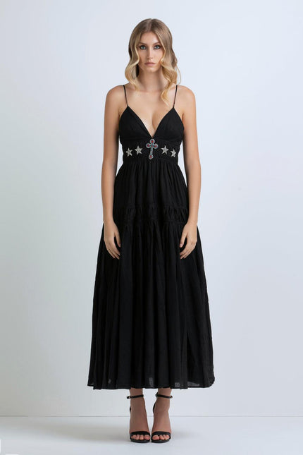 Woman wearing a black maxi dress with deep V-neck, jeweled cross and star detailing, thin straps