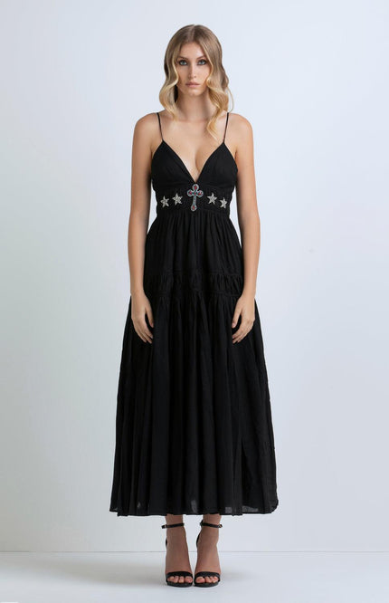 Woman wearing a black maxi dress with deep V-neck, jeweled cross and star detailing, thin straps