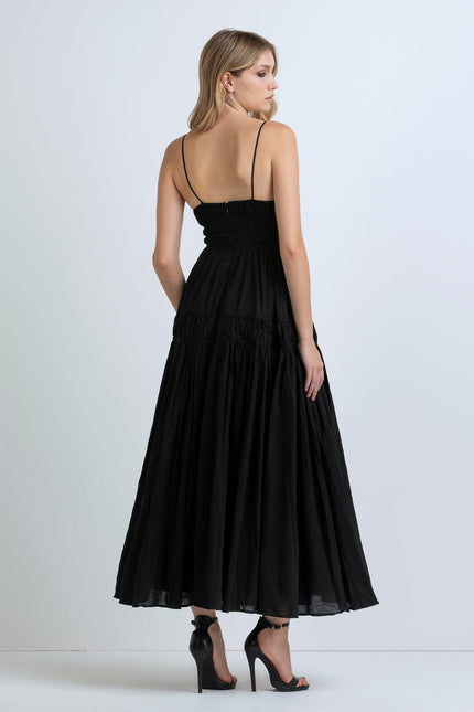 Woman in a black maxi dress with thin straps and high heels, shown from the back