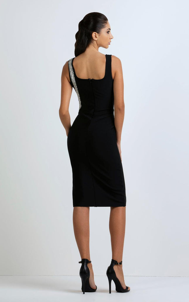 Woman in a black knee-length dress with a single embellished strap, standing in heels