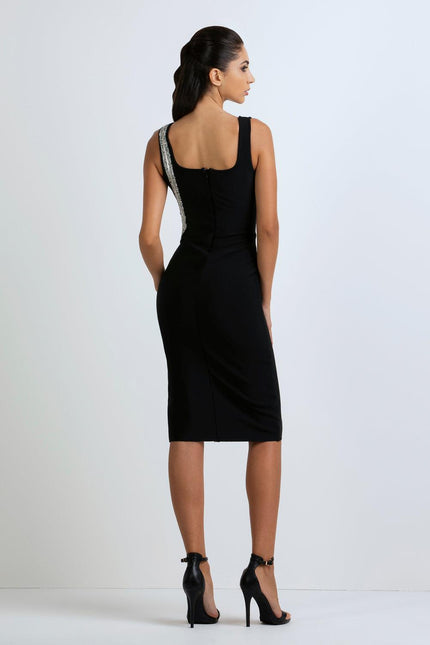 Woman in a black knee-length dress with a single embellished strap, standing in heels