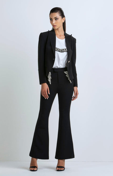 Woman wearing black flared pants, black blazer with sequin details, and white graphic tee