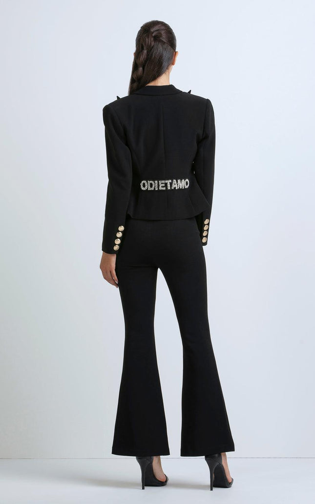 Woman in black flared pantsuit with crystal lettering on back, gold button details, high heels