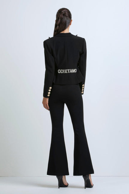 Woman in black flared pantsuit with crystal lettering on back, gold button details, high heels