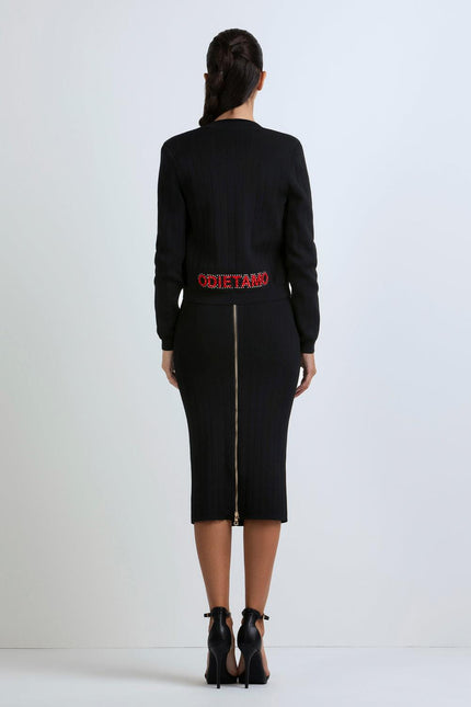 Woman wearing a fitted black ribbed midi dress with back gold zipper and red Odi et Amo lettering