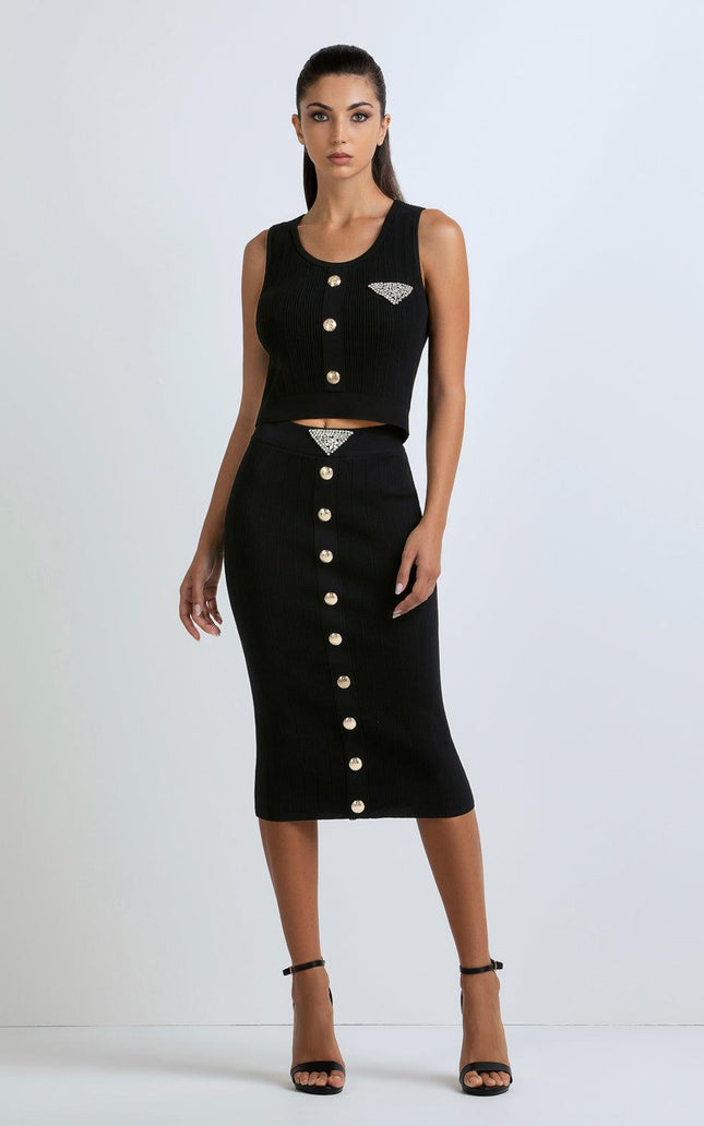 Woman wearing black sleeveless crop top and midi skirt set with gold buttons and rhinestone details