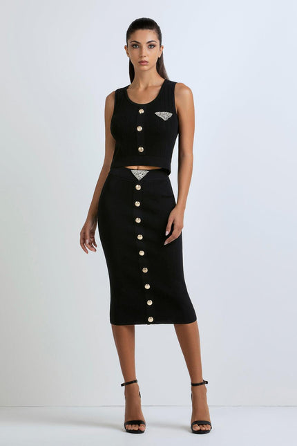 Woman wearing black sleeveless crop top and midi skirt set with gold buttons and rhinestone details