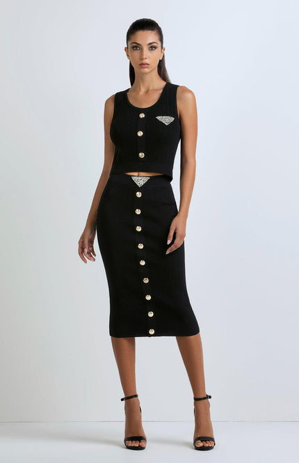 Woman in a black ribbed crop top and midi skirt set with gold buttons and rhinestone details