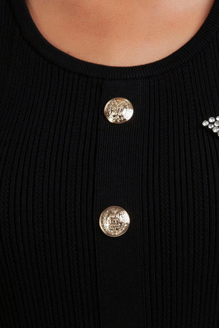 Close-up of black ribbed dress with gold buttons and rhinestone embellishment