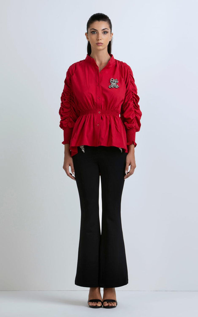 Woman wearing a red ruched sleeve blouse with embroidered detail and black flared pants