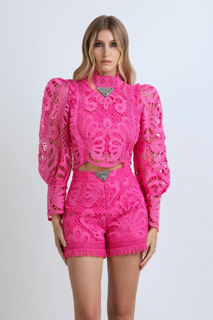 Woman wearing vibrant pink lace two-piece outfit with long sleeves and embellished details