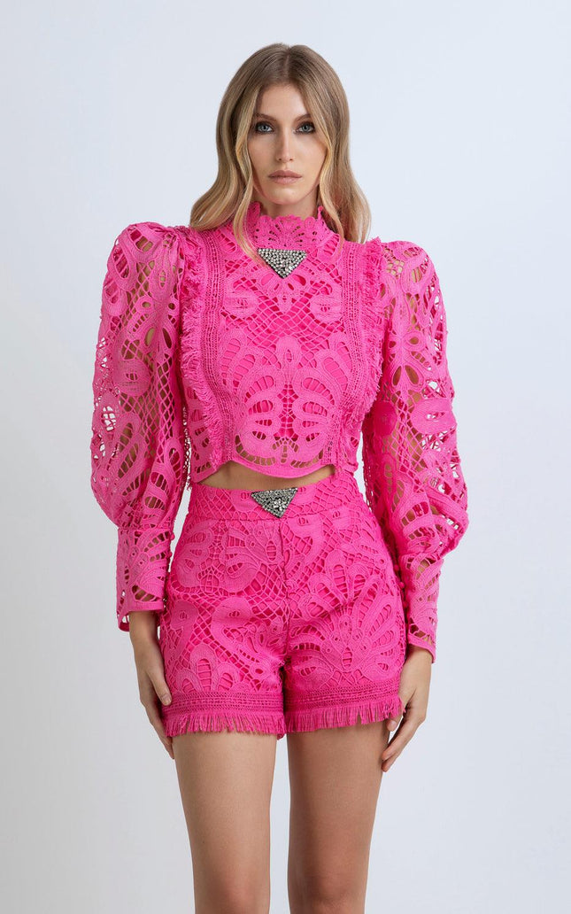 Woman in vibrant pink lace matching set with structured shoulders and fringed shorts