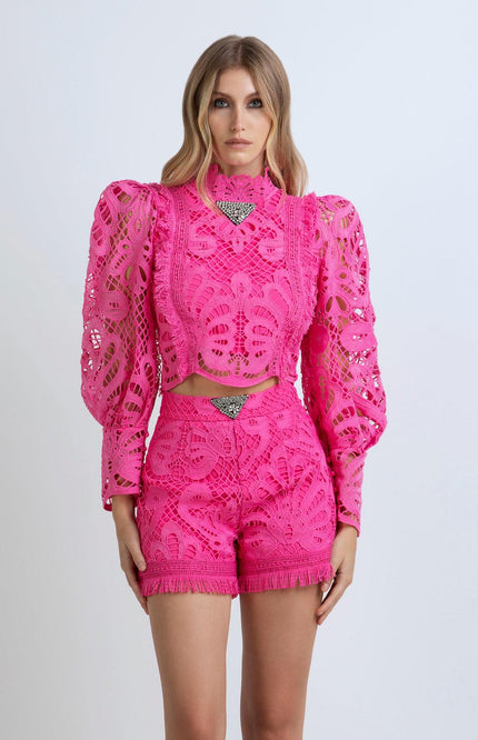 Woman in vibrant pink lace matching set with structured shoulders and fringed shorts
