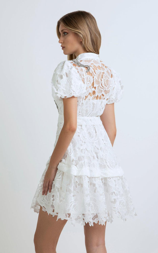 Woman wearing short white lace dress with puff sleeves and floral pattern, back view