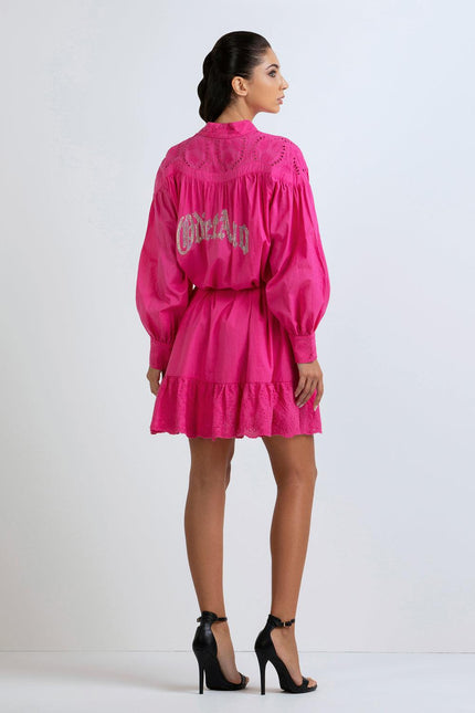 Woman in vibrant pink mini dress with embroidered back, long sleeves, and ruffle hem
