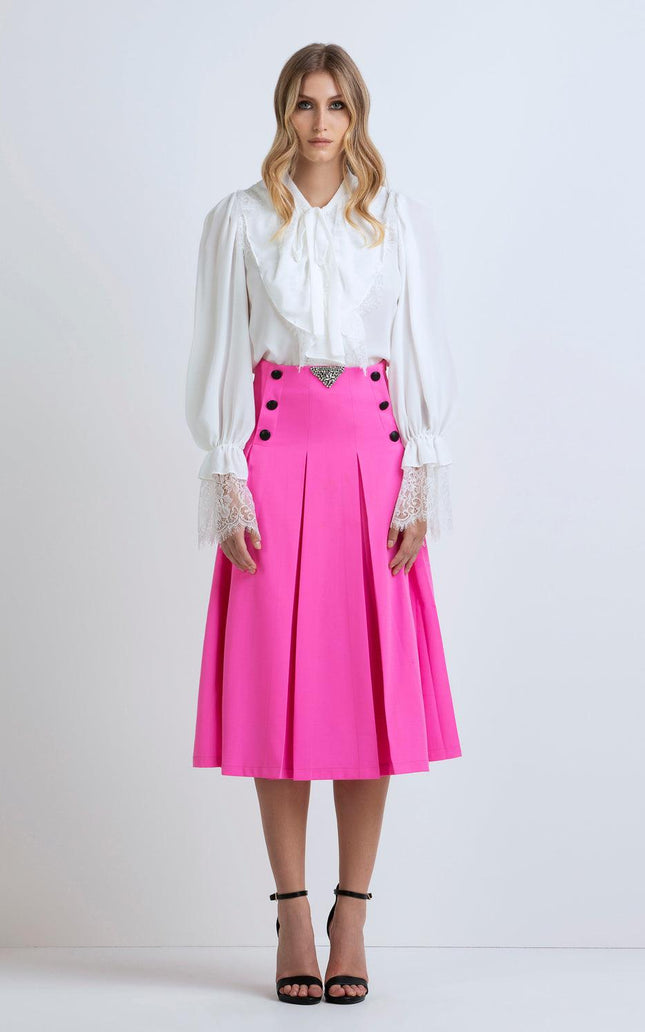 Woman wearing a white ruffled blouse and bright pink pleated midi skirt with black buttons