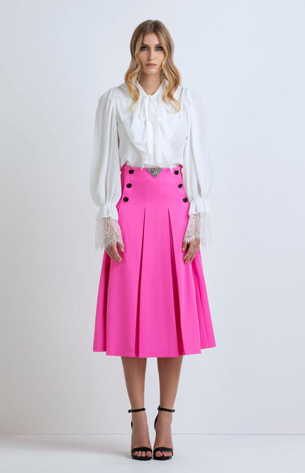 Woman wearing a white ruffled blouse and bright pink pleated midi skirt with black buttons