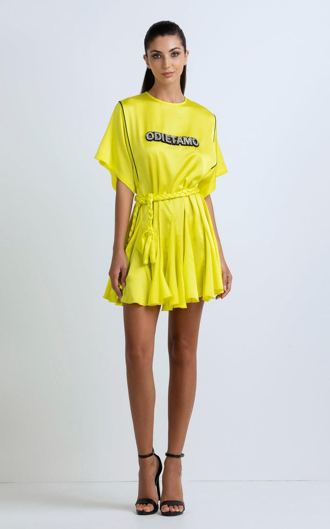 Woman wearing a bright yellow short dress with 'ODI ET AMO' text, braided belt, and black heels