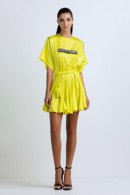 Woman wearing a bright yellow short dress with 'ODI ET AMO' text, braided belt, and black heels