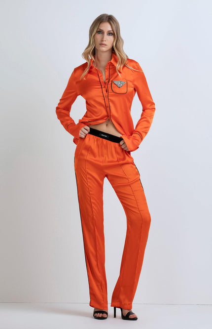 Woman wearing orange satin shirt and pants set with rhinestone pocket detail, fashion outfit