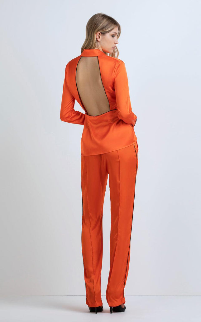 Woman wearing orange satin pantsuit with open back design and black trim, fashion outfit