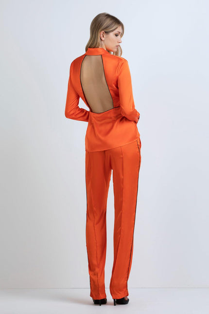 Woman wearing orange satin pantsuit with open back detail, standing in studio