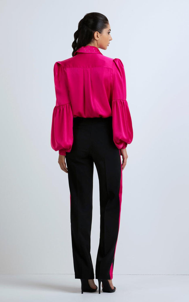 Woman wearing fuchsia satin blouse with puff sleeves and black pants with fuchsia sides