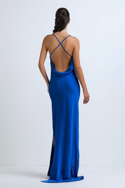 Woman in blue satin maxi dress with open back, criss-cross straps, and side slit