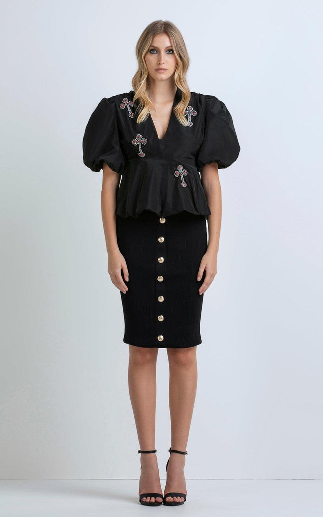 Woman in black puff-sleeve top with cross embellishments and black buttoned pencil skirt