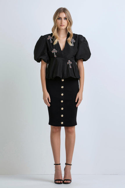 Woman in black puff-sleeve top with cross embellishments and black buttoned pencil skirt