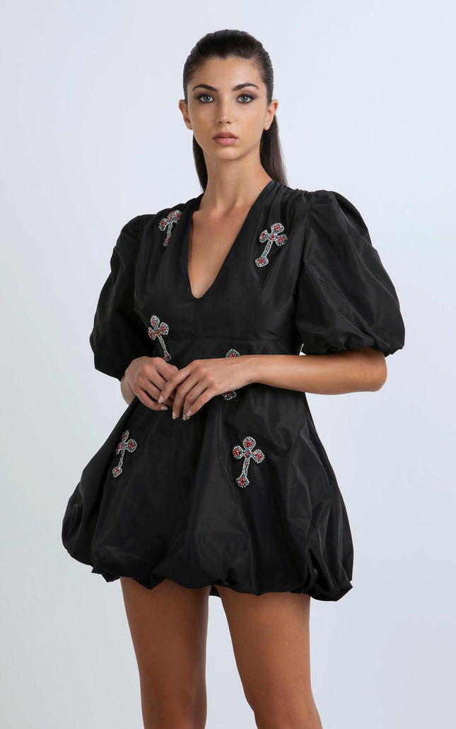 Woman wearing a black mini dress with puff sleeves and jeweled cross embellishments