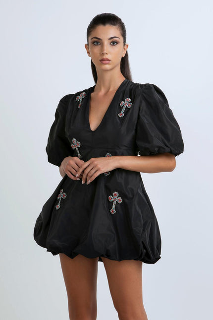 Woman wearing a black mini dress with puff sleeves and jeweled cross embellishments