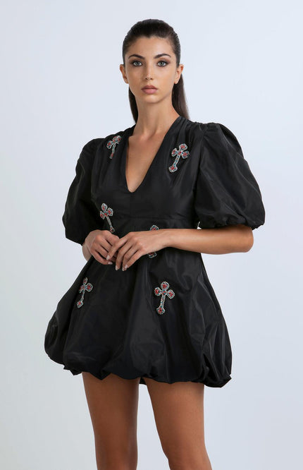 Woman wearing a black mini dress with puff sleeves and jeweled cross embellishments