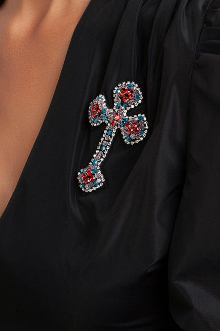 Black dress with deep neckline, featuring jeweled cross brooch in red, blue, and silver crystals