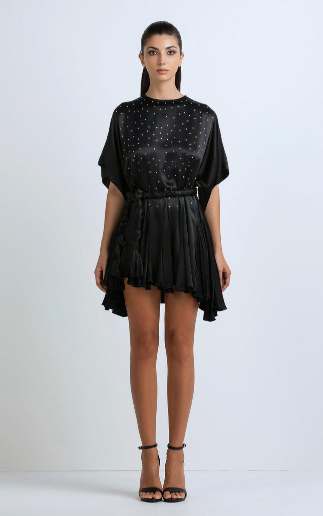 Woman wearing a black satin mini dress with studded details and a ruffled hem