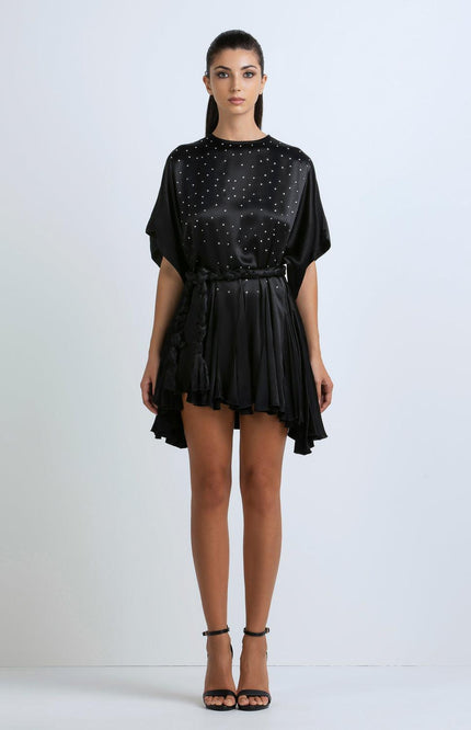 Woman wearing a black satin mini dress with studded details and a ruffled hem