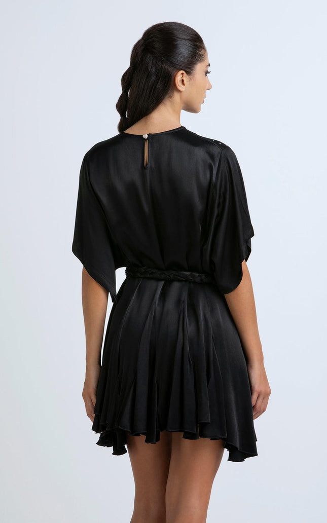 Woman in a short black satin dress with braided belt, back view, studio background