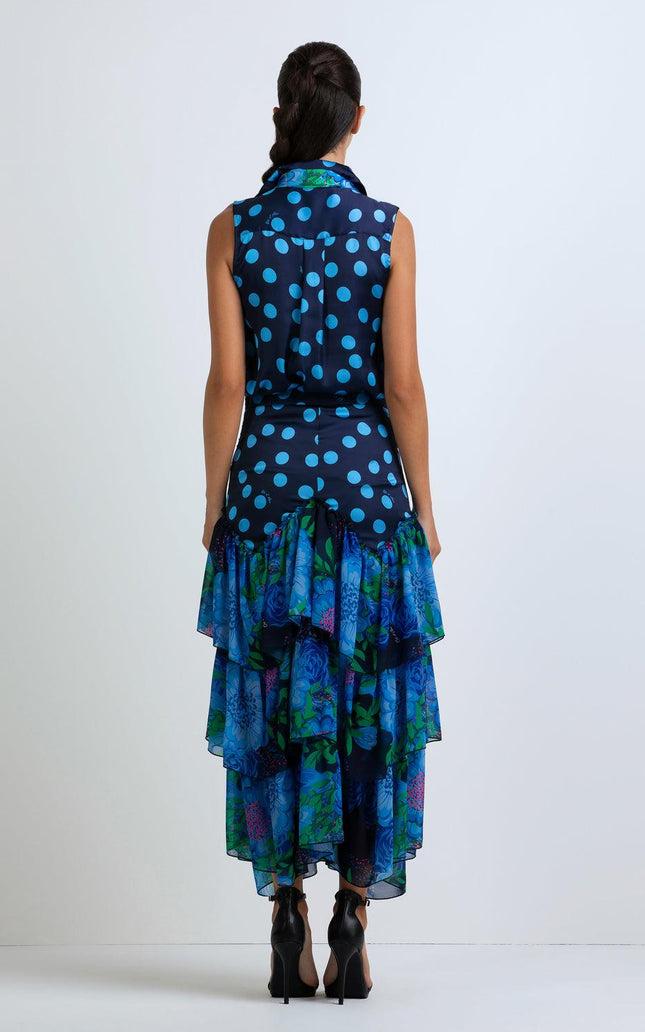 Woman in sleeveless blue polka dot blouse and layered floral ruffle skirt, back view.