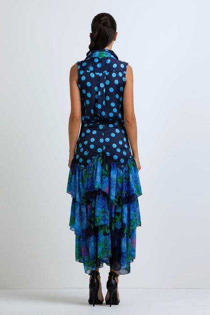 Woman in sleeveless navy blue polka dot top and layered floral ruffle skirt, back view