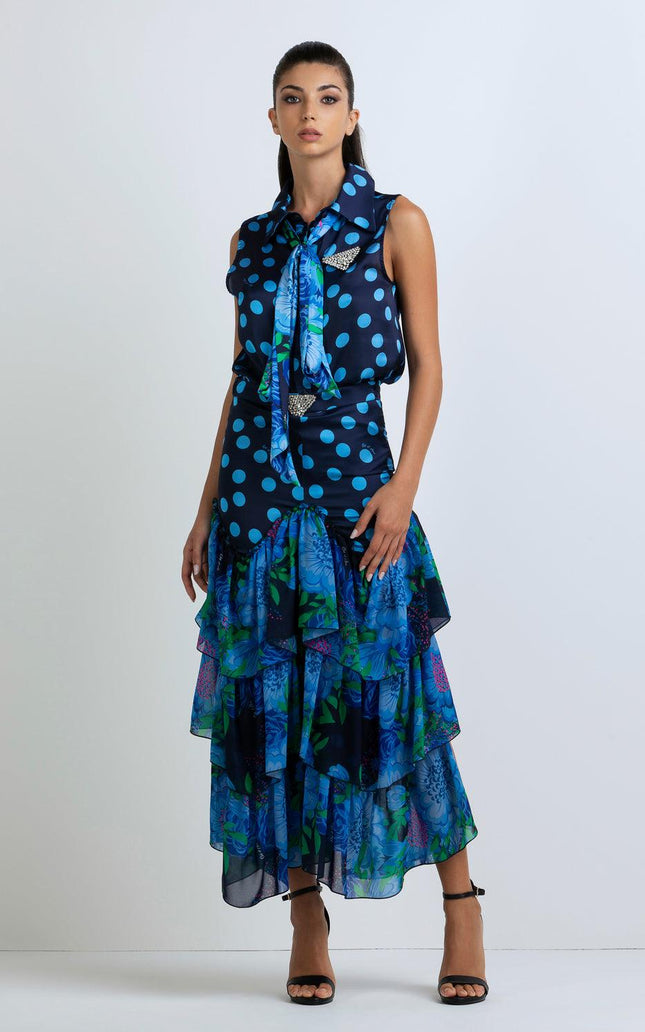 Woman in sleeveless blue polka dot blouse and tiered floral ruffle skirt, standing indoors