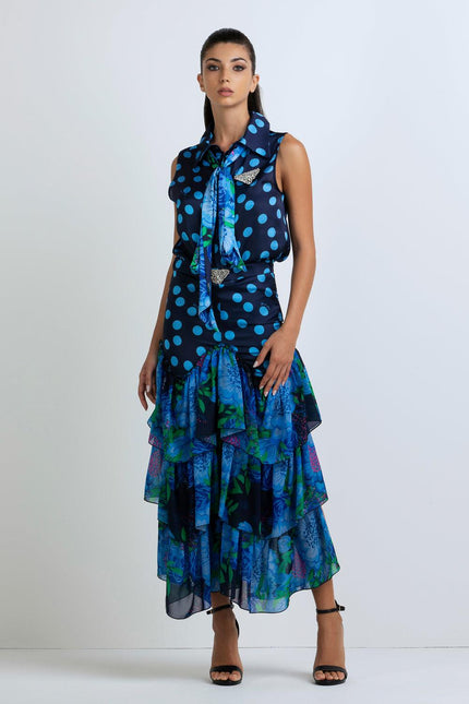 Woman in sleeveless blue polka dot blouse and tiered floral ruffle skirt, standing indoors