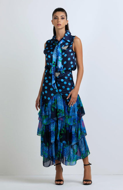 Woman in sleeveless blue polka dot blouse and tiered floral ruffle skirt, standing indoors